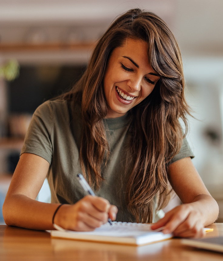 Photo of a smiling woman writing in a notebook for work