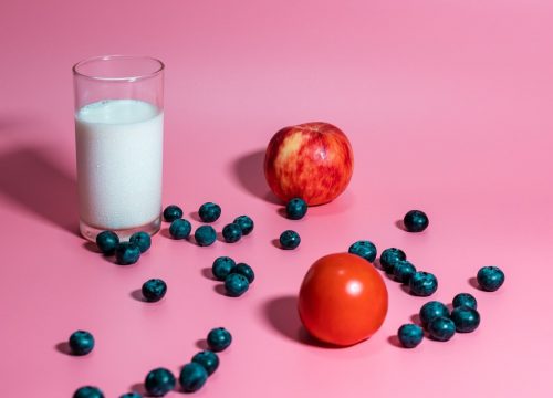 Photo of a glass of milk next to fruits and berries