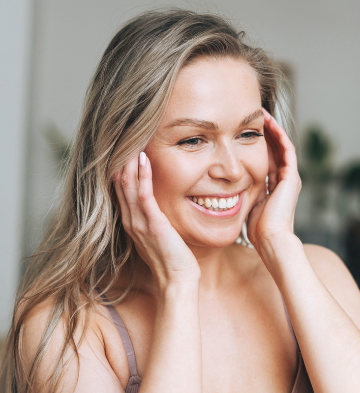 Photo of a blonde woman with great skin touching her face